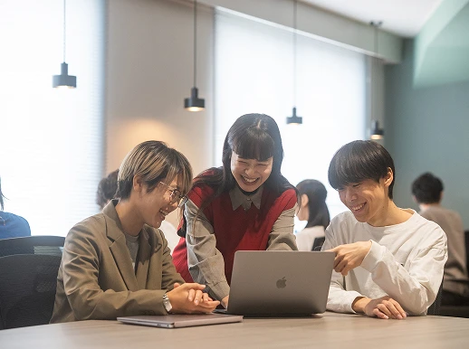 社員3名がノートパソコンを囲んで笑顔で話し合っている様子