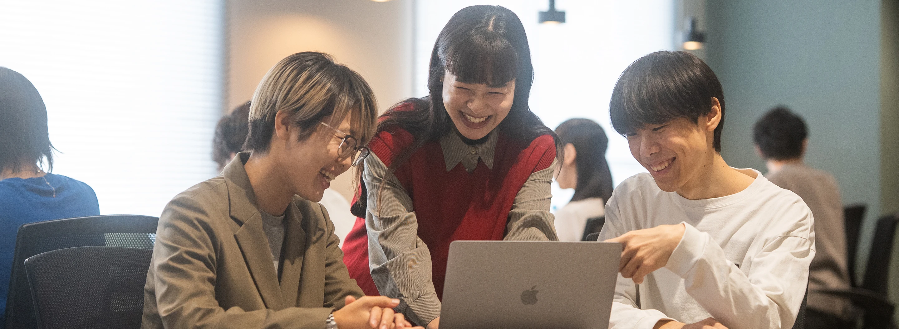 社員3名がノートパソコンを囲んで笑顔で話し合っている様子